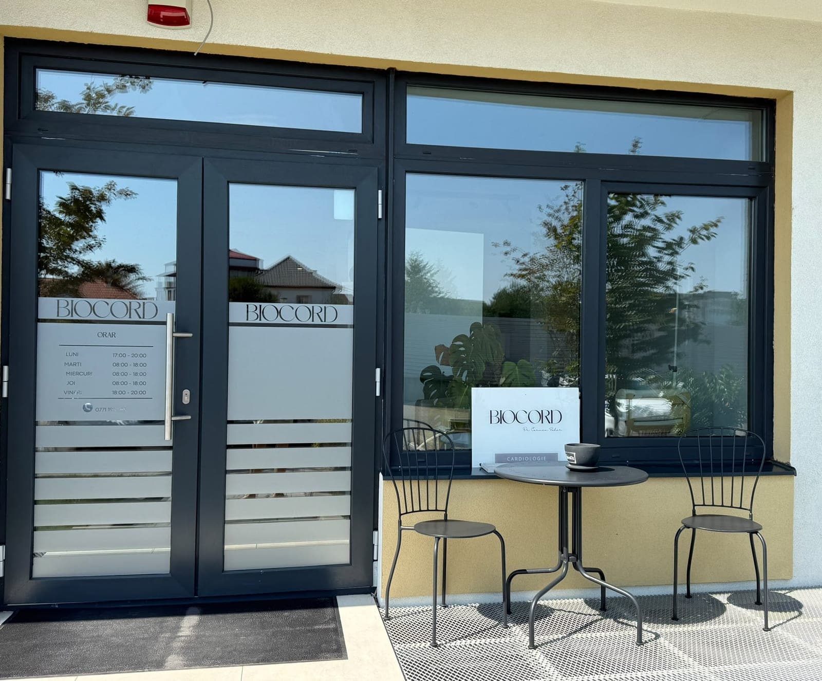 Intrarea în cabinetul Biocord, cu ușa de sticlă inscripționată și o masă cu scaune în față